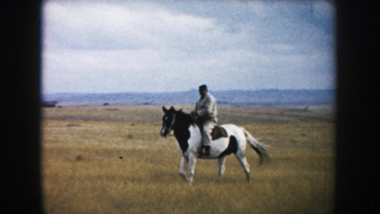 An adult rider in light clothing and a dark hat rides a black-and-white pinto horse across South Dakota prairie, based on clip metadata.
