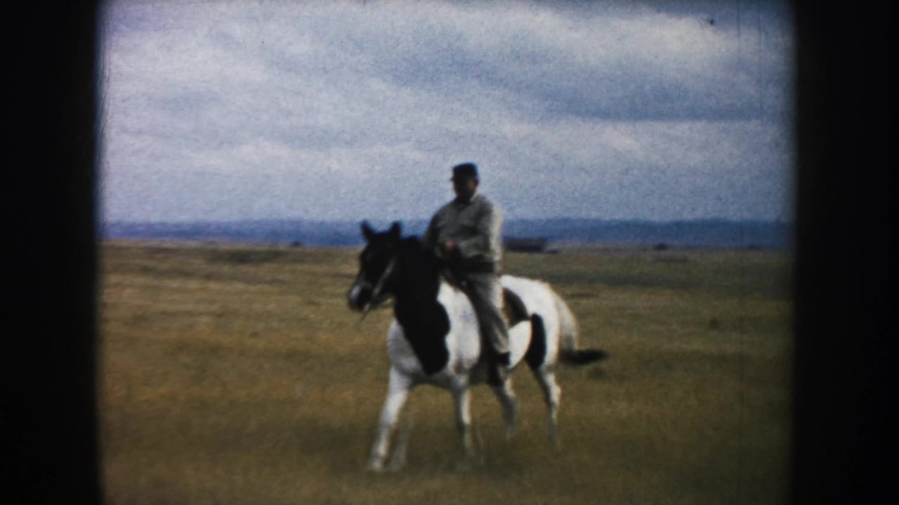 An adult rider on a black-and-white pinto horse approaches through dry South Dakota prairie in vintage 8mm home-movie footage.