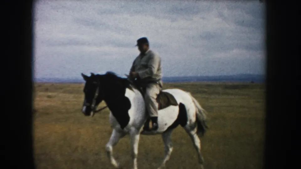 The mounted man continues across a South Dakota prairie on a black-and-white pinto horse, framed by 8mm film borders.