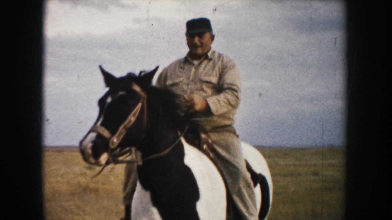 Man in a cap riding a black-and-white pinto horse on open prairie.