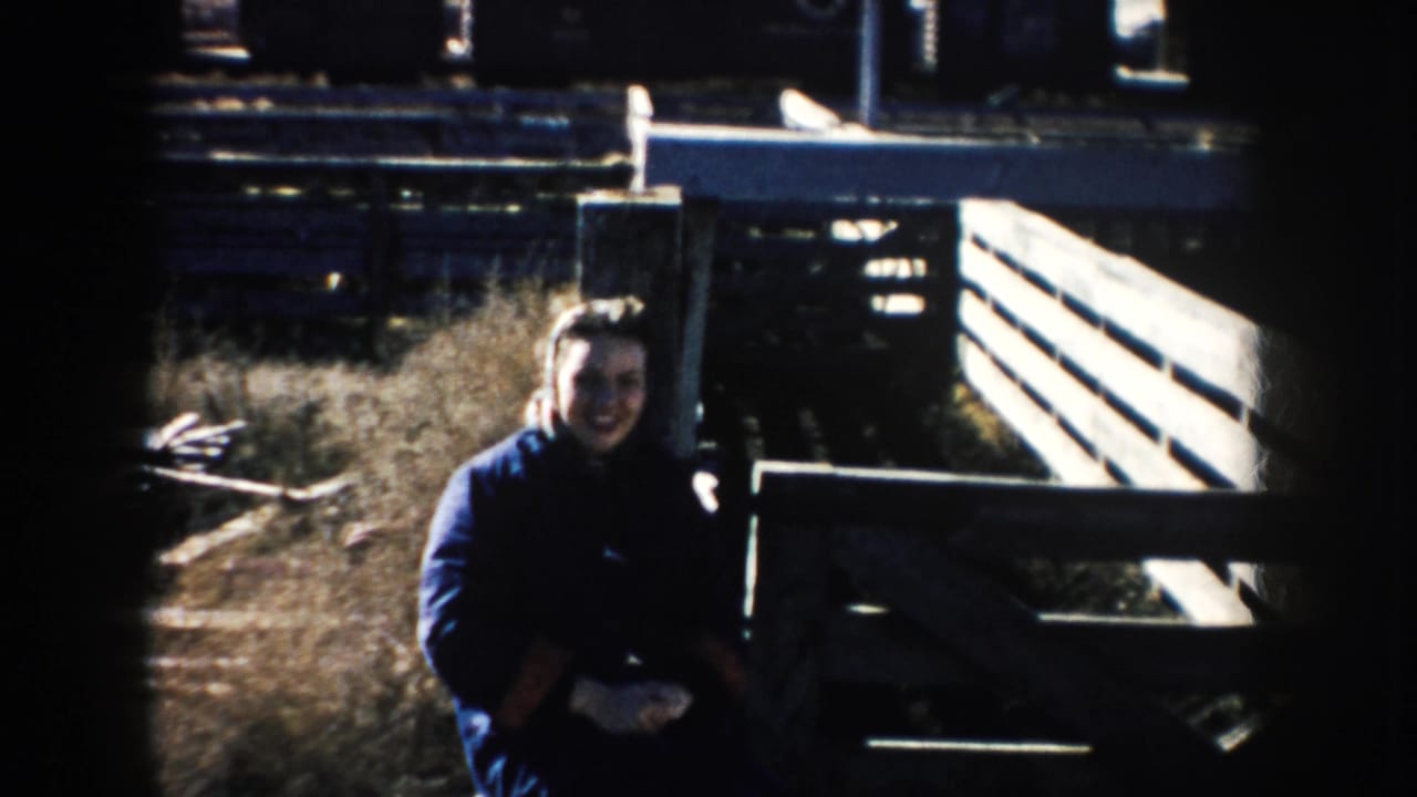 Woman in a dark coat smiles beside a wooden cattle pen.