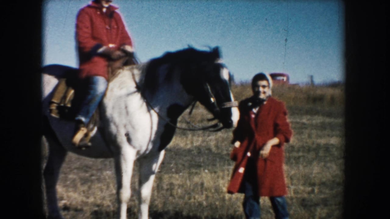 A man remains mounted on the white horse while the woman in red stands nearby, both framed by a grassy South Dakota field.