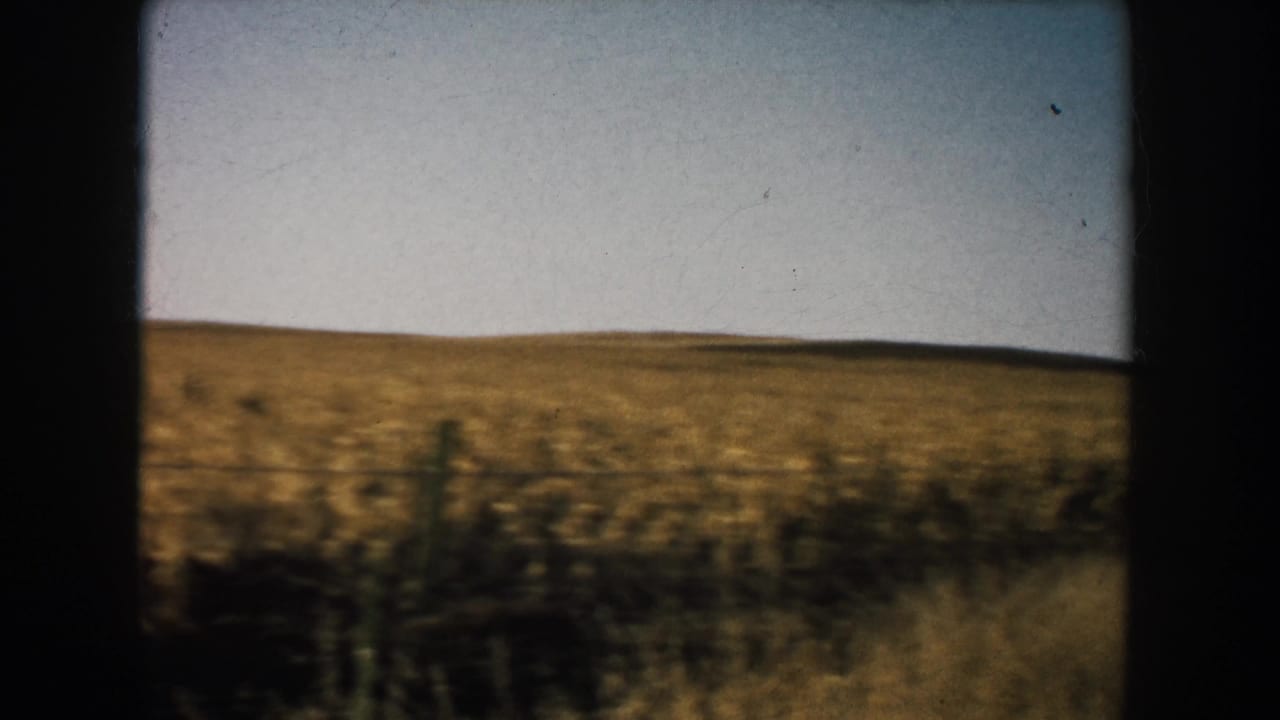 1953 South Dakota farm field with a low horizon, pale sky, and dark film-frame borders from the 8mm scan.