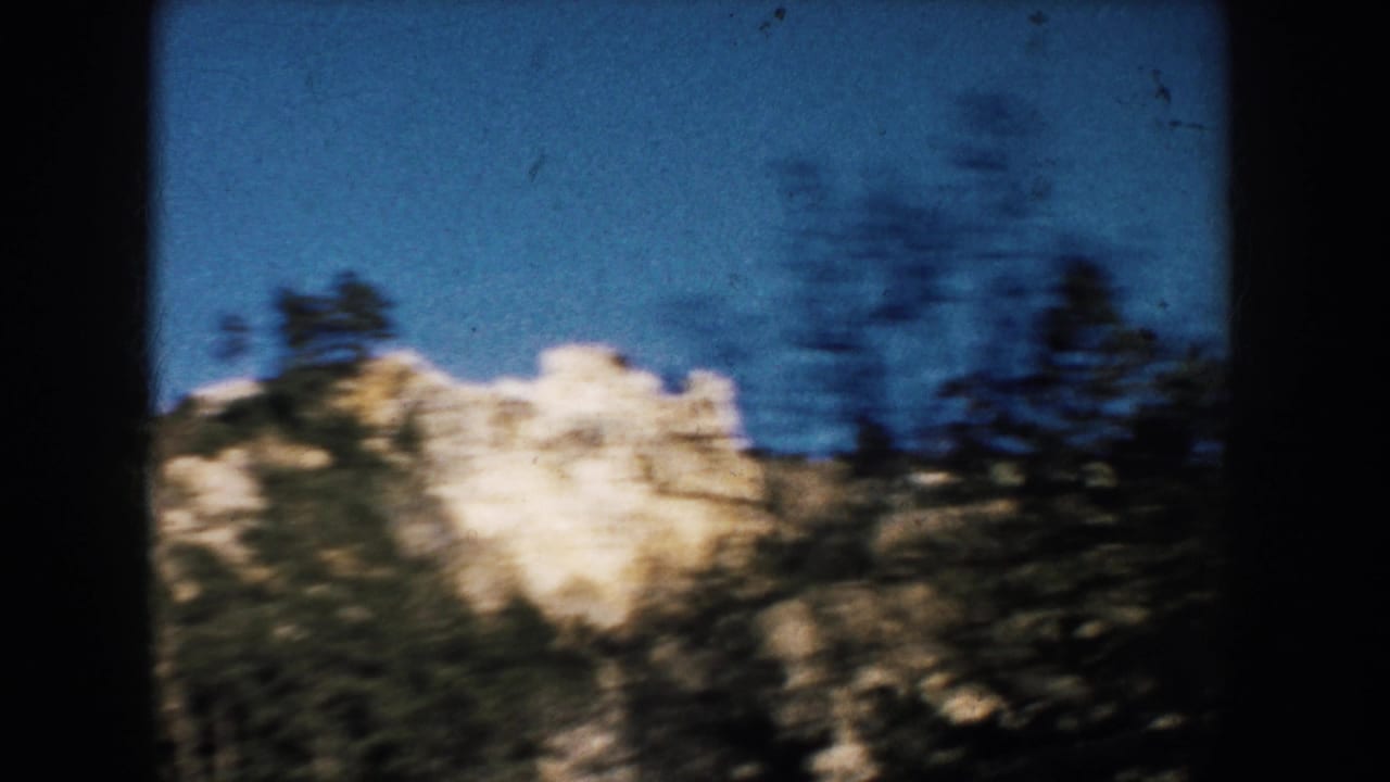 1953 South Dakota 8mm frame showing a pale rocky cliff and pines seen in motion from a vehicle.