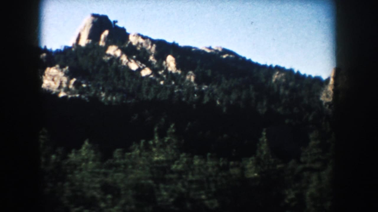 Pale rock ridge above a dark evergreen forest under blue sky.