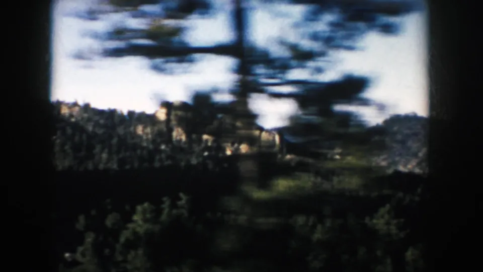 1953 South Dakota 8mm frame where foreground trees frame pale rock outcrops above a dark evergreen forest.