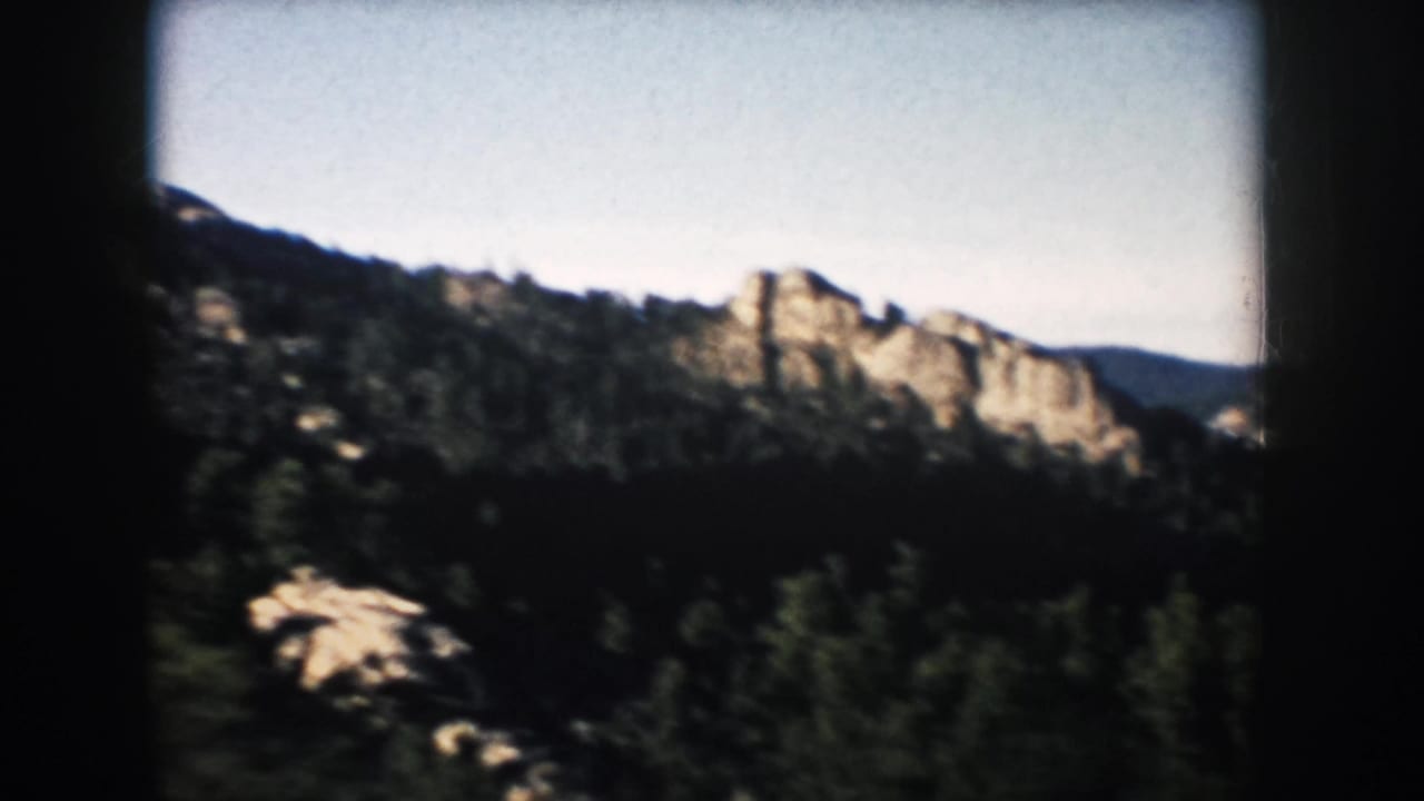 Evergreen hills and brown rock formations seen through a dark 8mm film frame.