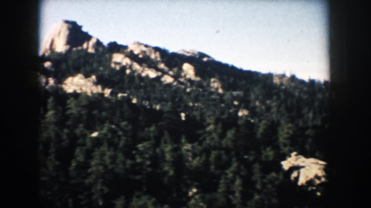 1953 South Dakota travel frame with a prominent rocky outcrop rising above evergreen forest.