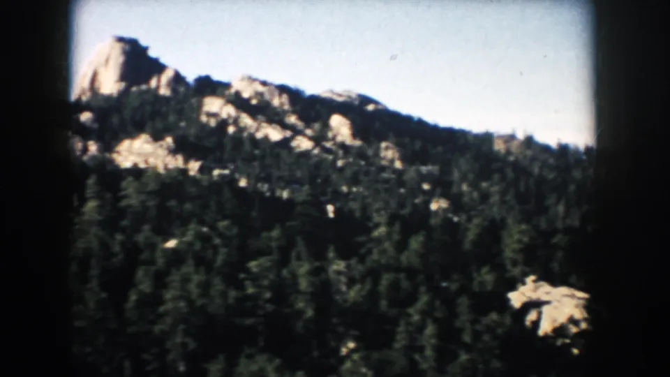 1953 South Dakota travel frame with a prominent rocky outcrop rising above evergreen forest.