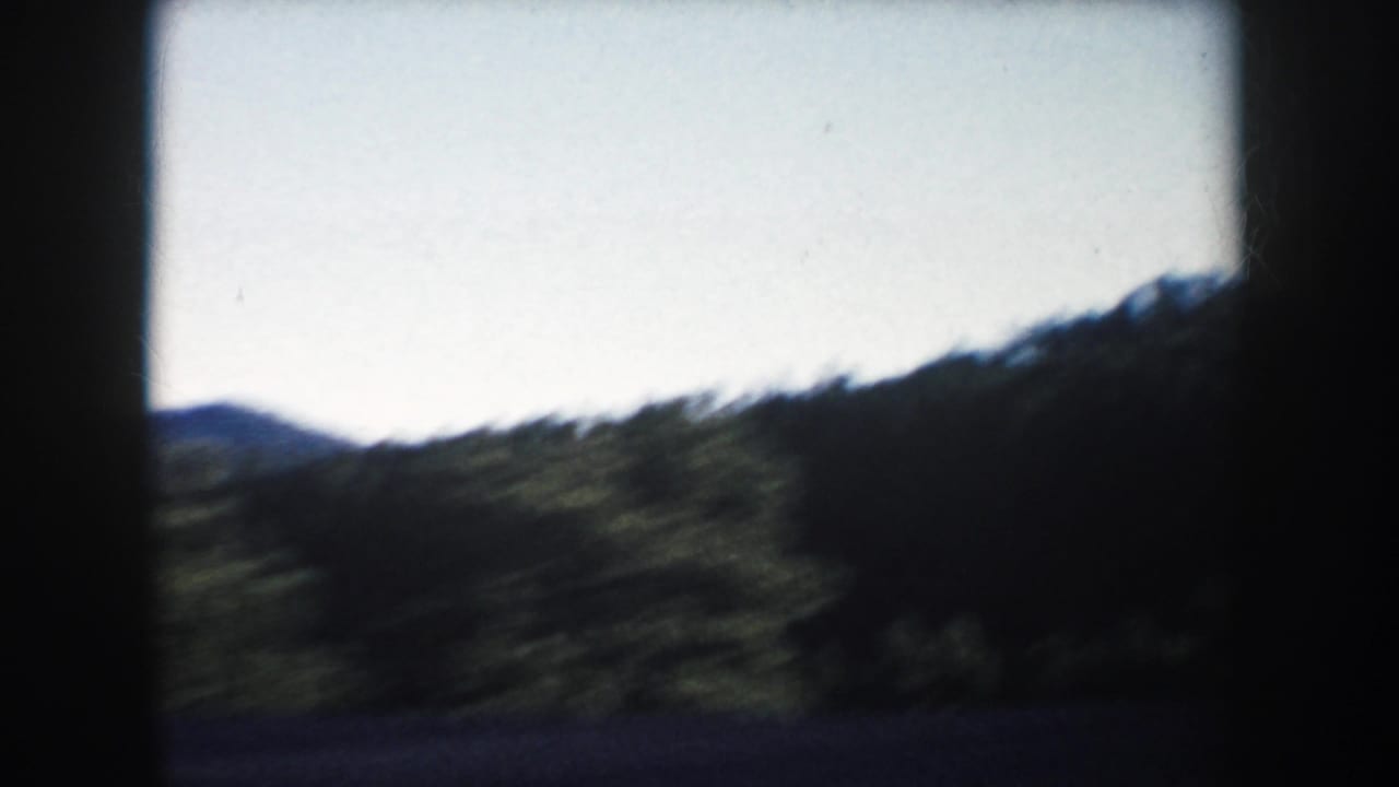 1953 South Dakota 8mm frame with a dark, motion-blurred hillside and distant ridge under open sky.