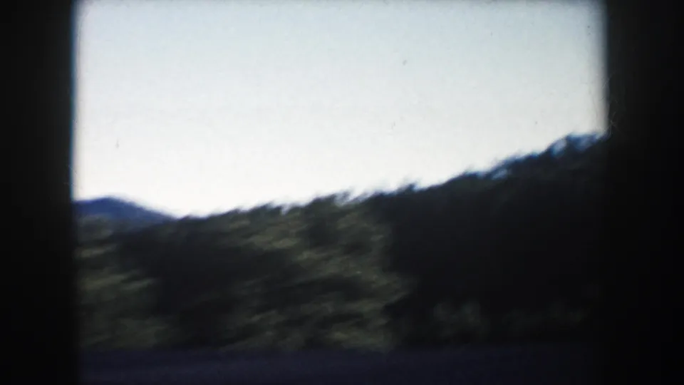 1953 South Dakota 8mm frame with a dark, motion-blurred hillside and distant ridge under open sky.