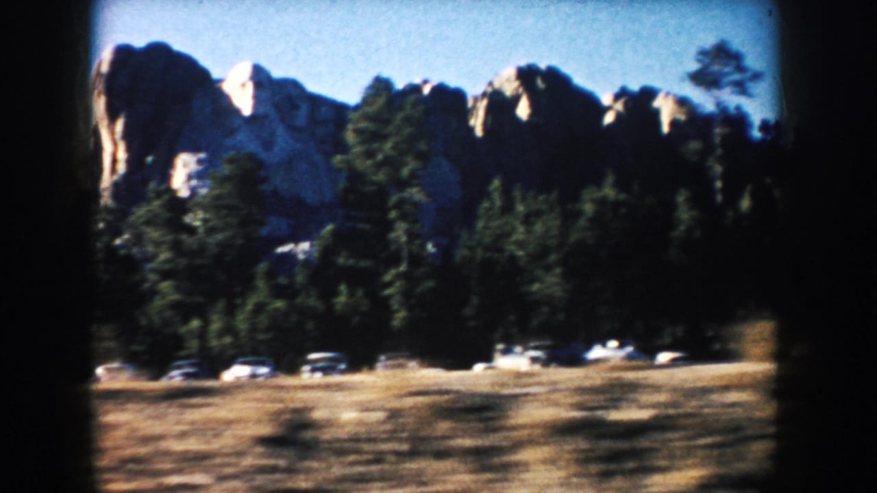 1953 8mm frame showing Mount Rushmore above forest and parked cars in South Dakota.