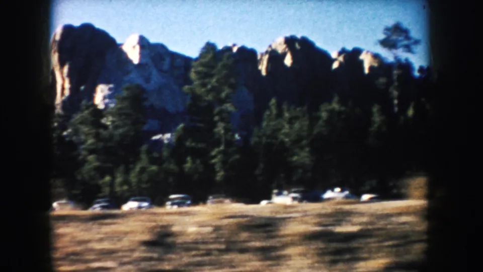 1953 8mm frame showing Mount Rushmore above forest and parked cars in South Dakota.