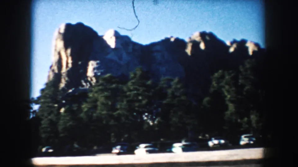 1953 South Dakota home-movie view of Mount Rushmore rising above trees and a small parking area with mid-century cars.