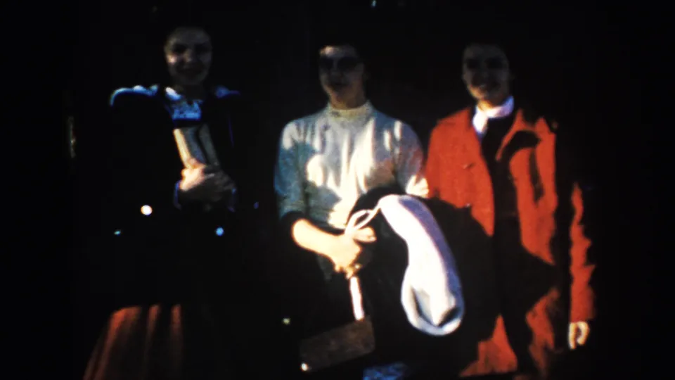 Three adult visitors pose in dark shadow and bright sun during a 1953 South Dakota home-movie travel stop.