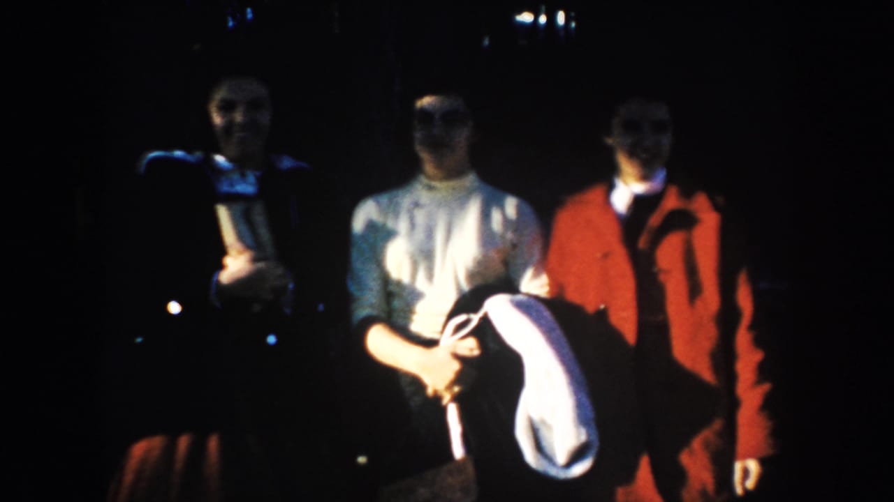 Adults in mid-century clothing pose for an 8mm home-movie camera, with strong shadow obscuring some facial detail.