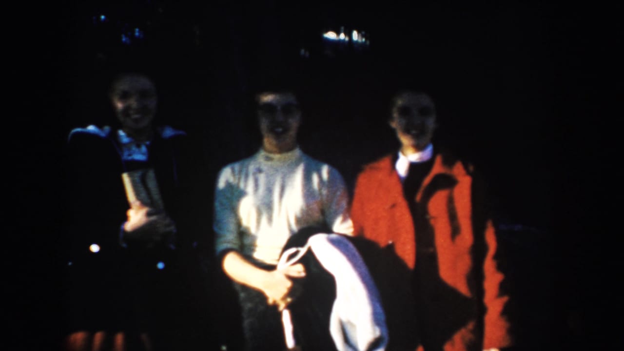 Three adult visitors stand shoulder to shoulder in 1953 South Dakota travel footage, their clothing and faces softened by exposure.