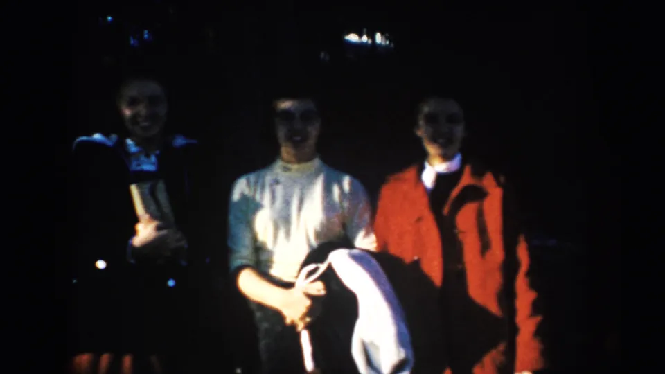 Three adult visitors stand shoulder to shoulder in 1953 South Dakota travel footage, their clothing and faces softened by exposure.