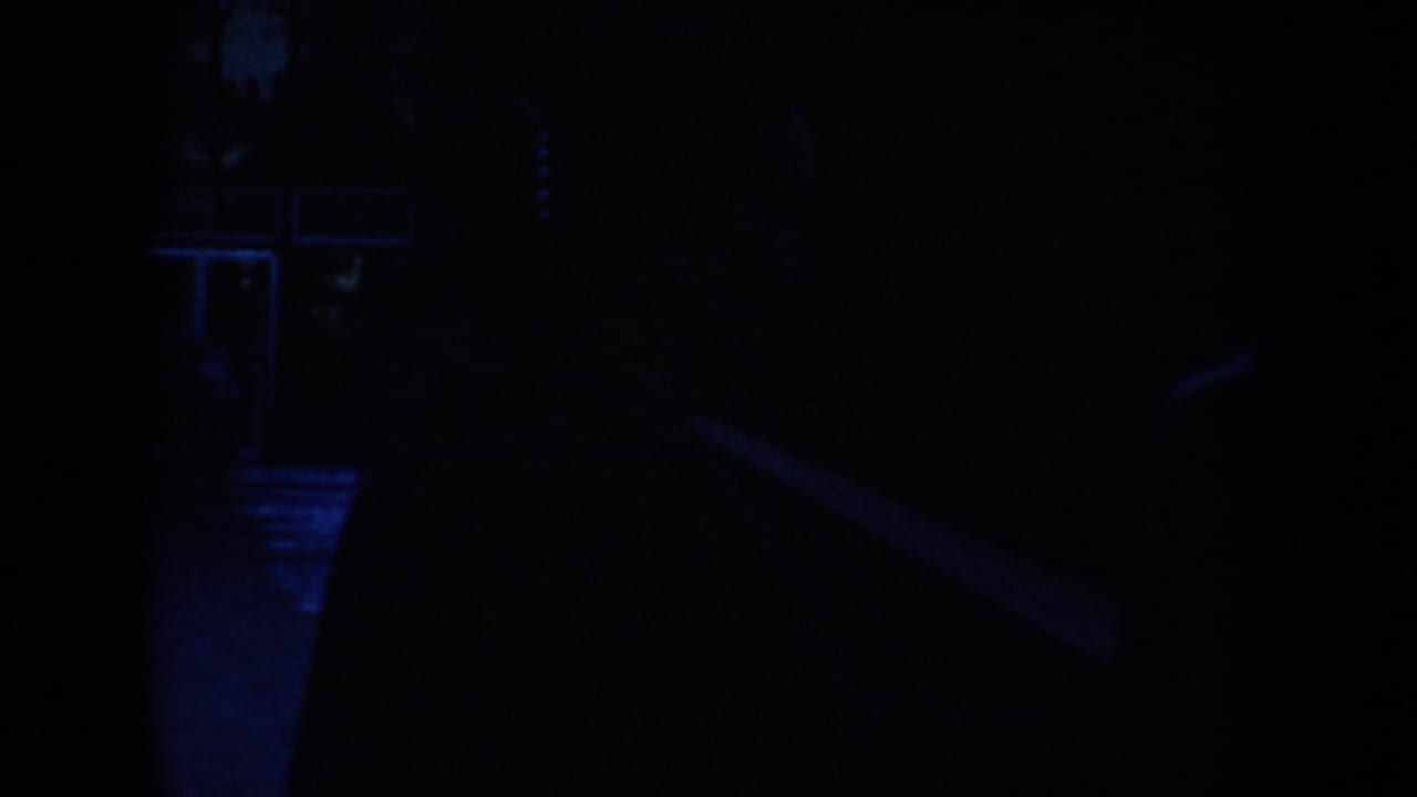 Very dark blue-lit frame with faint silhouettes and an interior edge at left.