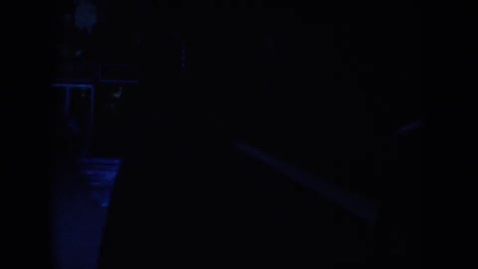 1953 South Dakota 8mm frame with barely visible figures or forms in a blue-lit nighttime interior or shaded space.