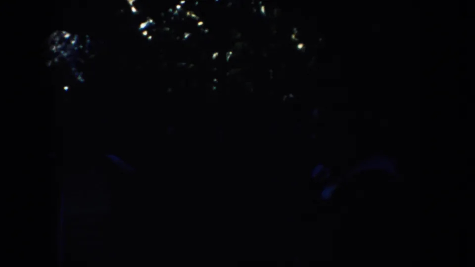 Dark opening frame from a 1953 8mm South Dakota travel clip, with only faint tree shapes visible before the monument appears.