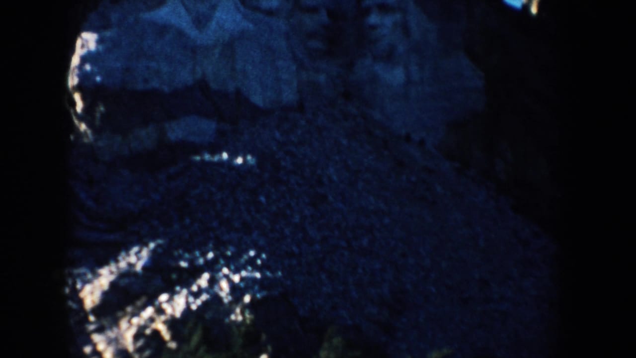 1953 8mm view of Mount Rushmore in South Dakota, with carved stone features partly visible in deep blue shadow.