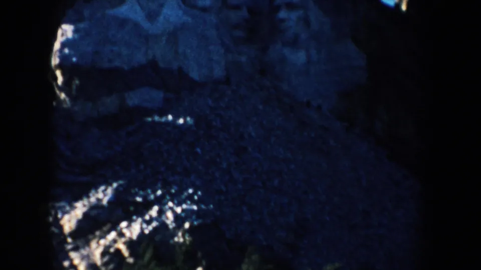 1953 8mm view of Mount Rushmore in South Dakota, with carved stone features partly visible in deep blue shadow.