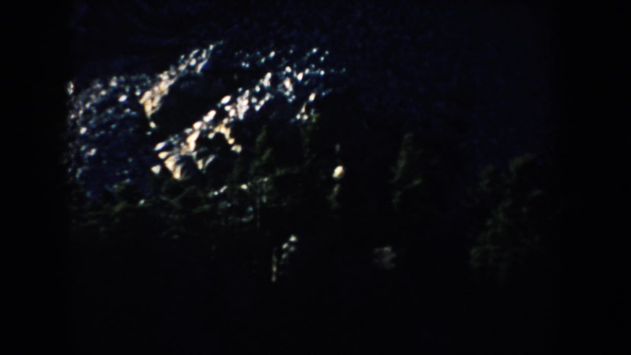 Blue-cast 1953 8mm view of Mount Rushmore rock forms, with bright stone highlights and dark forested areas below.