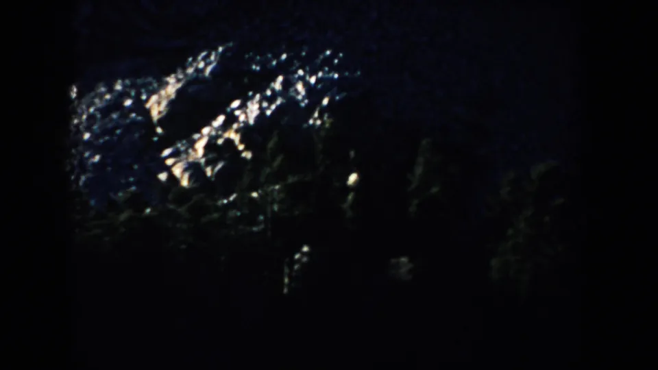 Blue-cast 1953 8mm view of Mount Rushmore rock forms, with bright stone highlights and dark forested areas below.