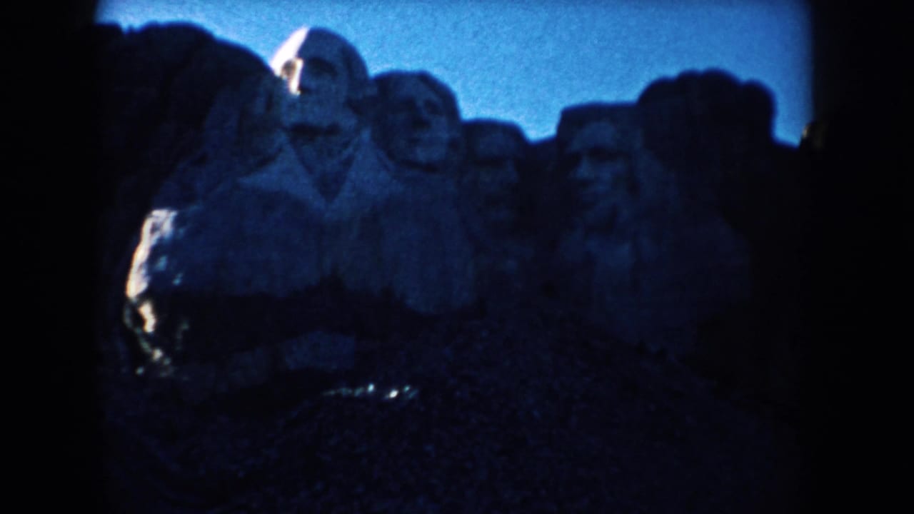 Mount Rushmore stone faces under a blue sky, partly darkened by shadow and film edges.