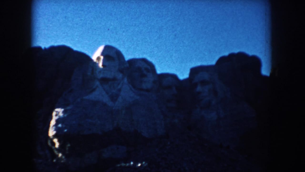 1953 home-movie frame of Mount Rushmore's presidential carvings, with soft focus, blue cast, and dark exposure.