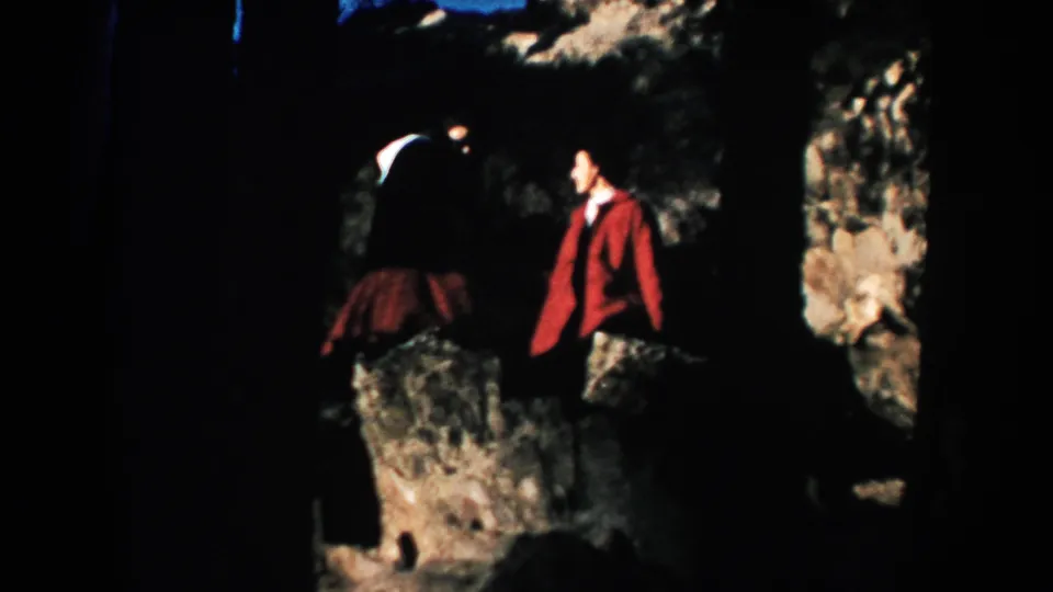 A woman in a dark outfit and a man in a red jacket stand amid boulders in this South Dakota home-movie frame.