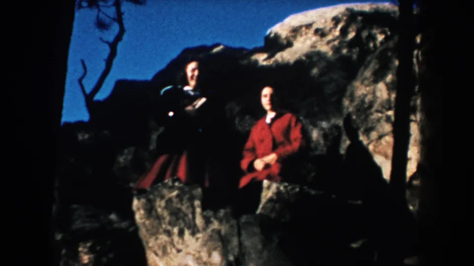 Two adults pose near boulders and trees, with a woman in a red coat visible against the rocky South Dakota setting.