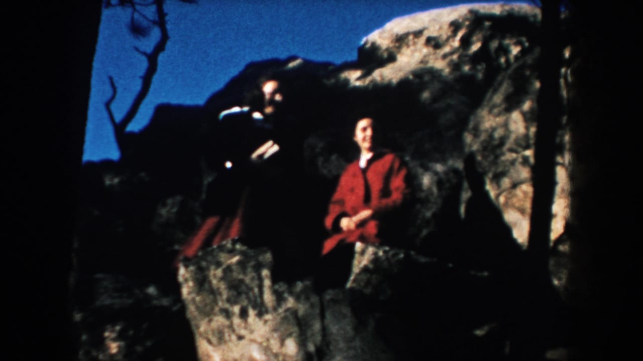 1953 South Dakota 8mm frame showing two people posed among rocks in a wooded area with deep shadows and blue sky.