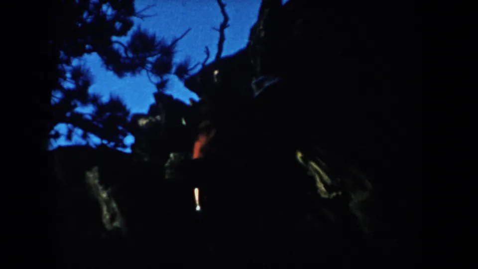 South Dakota 8mm home-movie frame from 1953 with two shadowed figures moving through dark woods at twilight.