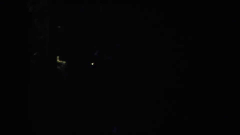 A very underexposed 1953 South Dakota night frame with indistinct vertical shapes and isolated yellow-blue highlights.