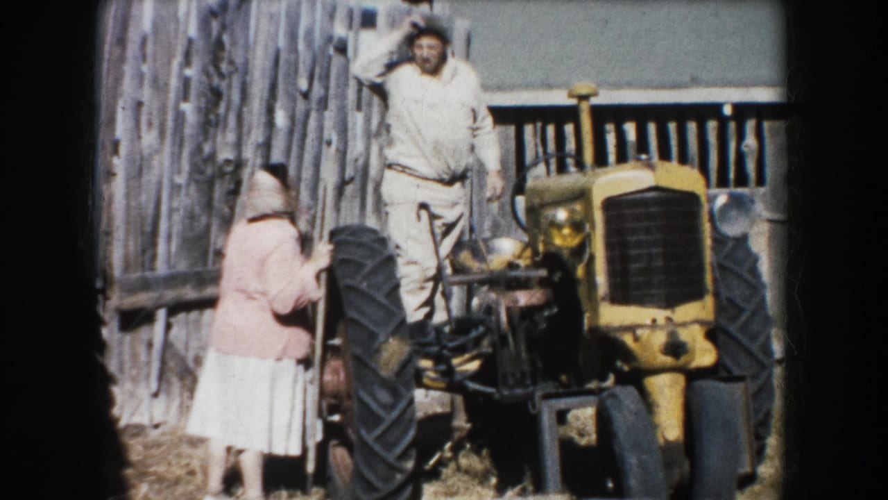 An adult man and woman are seen with a yellow tractor by a wood fence in 1953 South Dakota farm footage.