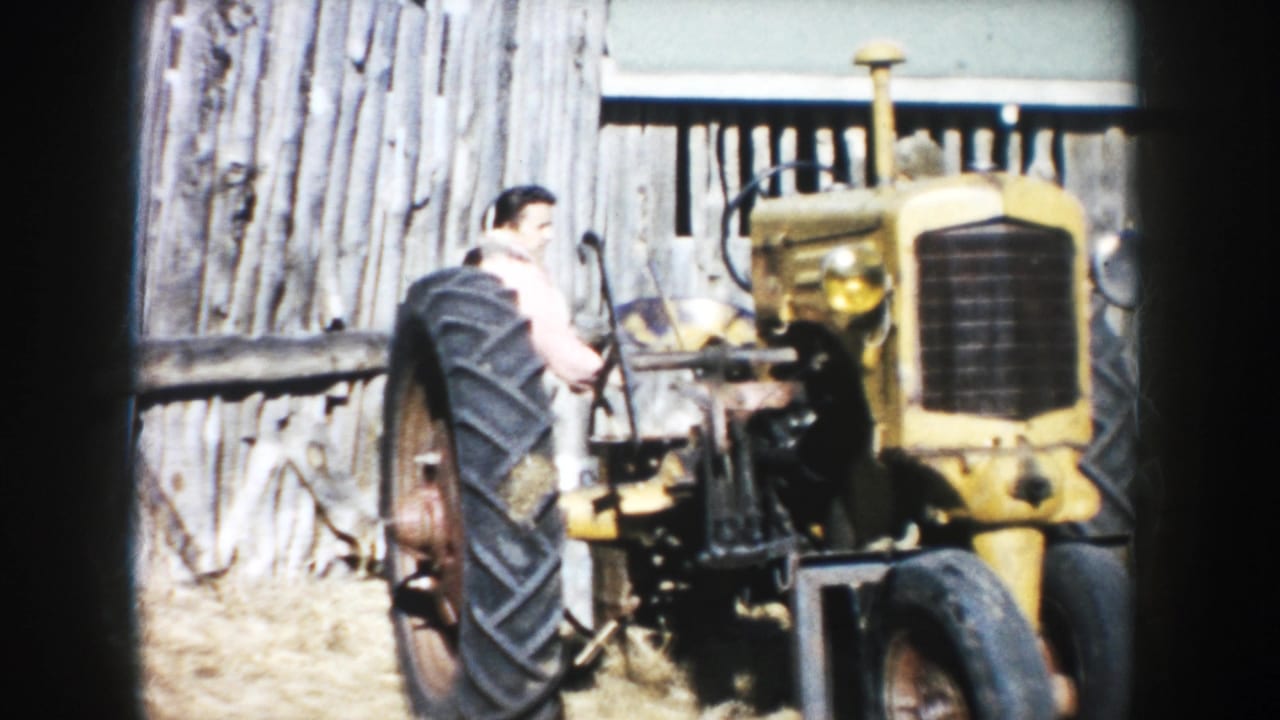 1953 South Dakota farm scene with a man beside a yellow tractor in front of a weathered wooden barn wall.