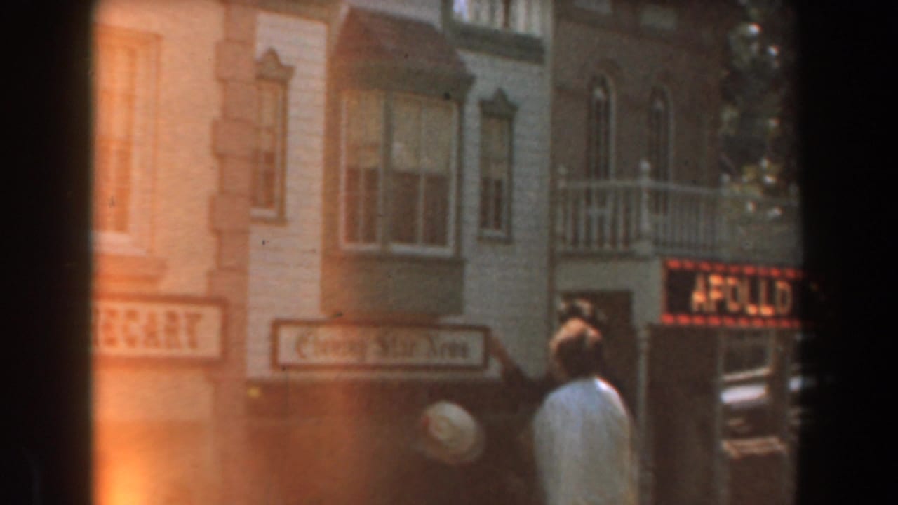 Visitors walk past old-fashioned storefronts with an apothecary sign and upper windows.