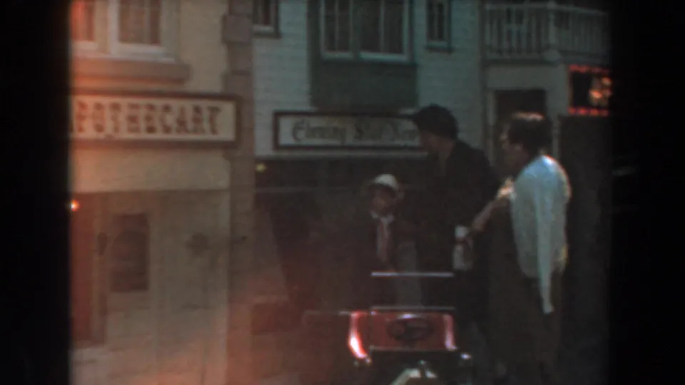 At the 1961 Knott's Berry Farm street set, adults pause near a red stroller or cart with apothecary and other storefront signs behind them.