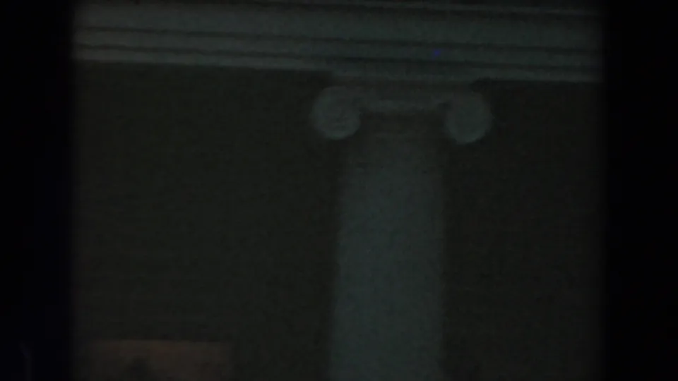 Low-light 8mm frame from the Knott's Berry Farm scene showing a column base, brick surface, and heavy film-edge shadow.