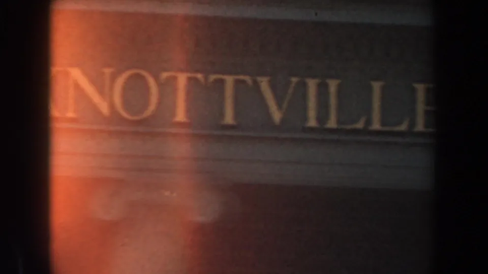Close view of a themed facade at Knott's Berry Farm with partial gold letters reading NOTTVILLE and a classical column below.