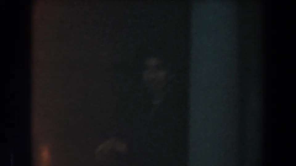 Low-light home-movie frame from Knott's Berry Farm showing a faint visitor shape inside a dark interior space.
