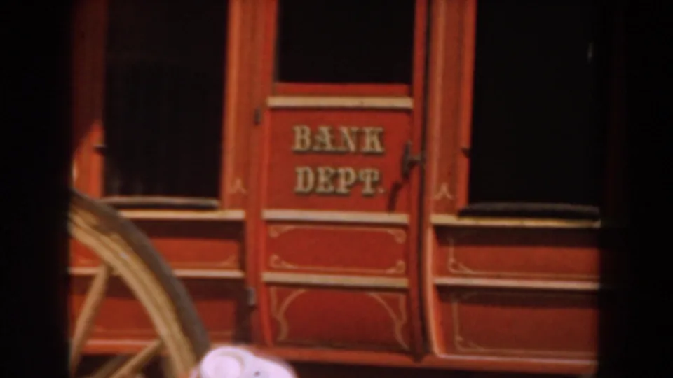 A red Knott's Berry Farm rail car door with gold Bank Dept. lettering passes the camera, with part of a wheel visible below.