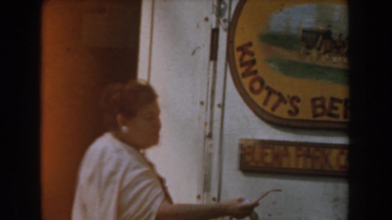 A woman in a light-colored dress stands near the Knott's Berry Farm sign in this 1961 Buena Park home-movie frame.