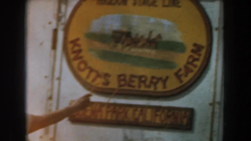 A visitor's hand points toward the yellow Knott's Berry Farm sign and Buena Park, California plaque in 1961 footage.