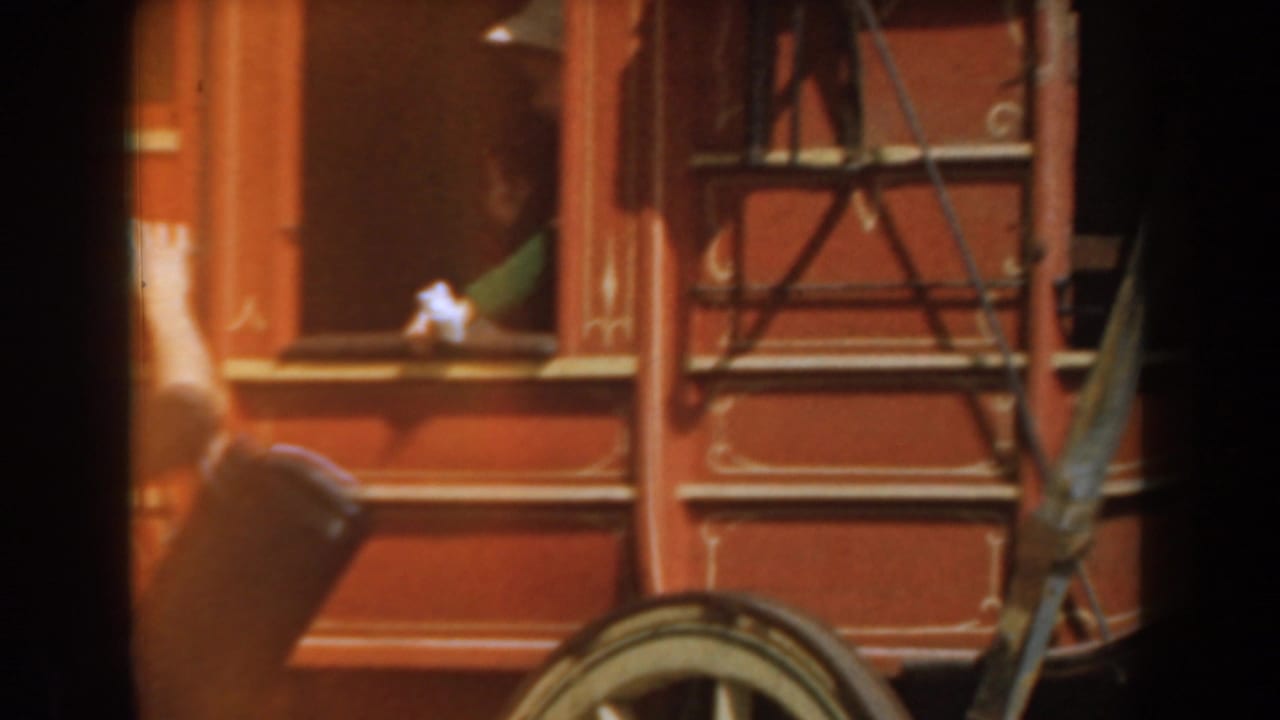 Woman in a hat leaning from the window of a red stagecoach.