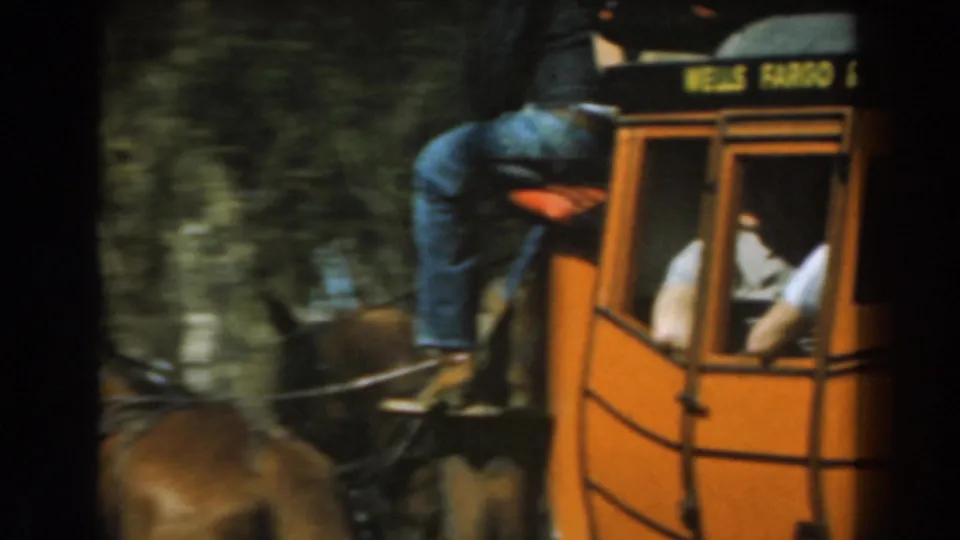 Side of the Knott's Berry Farm stagecoach with a rider seated above, passengers inside, and horses partly visible below.