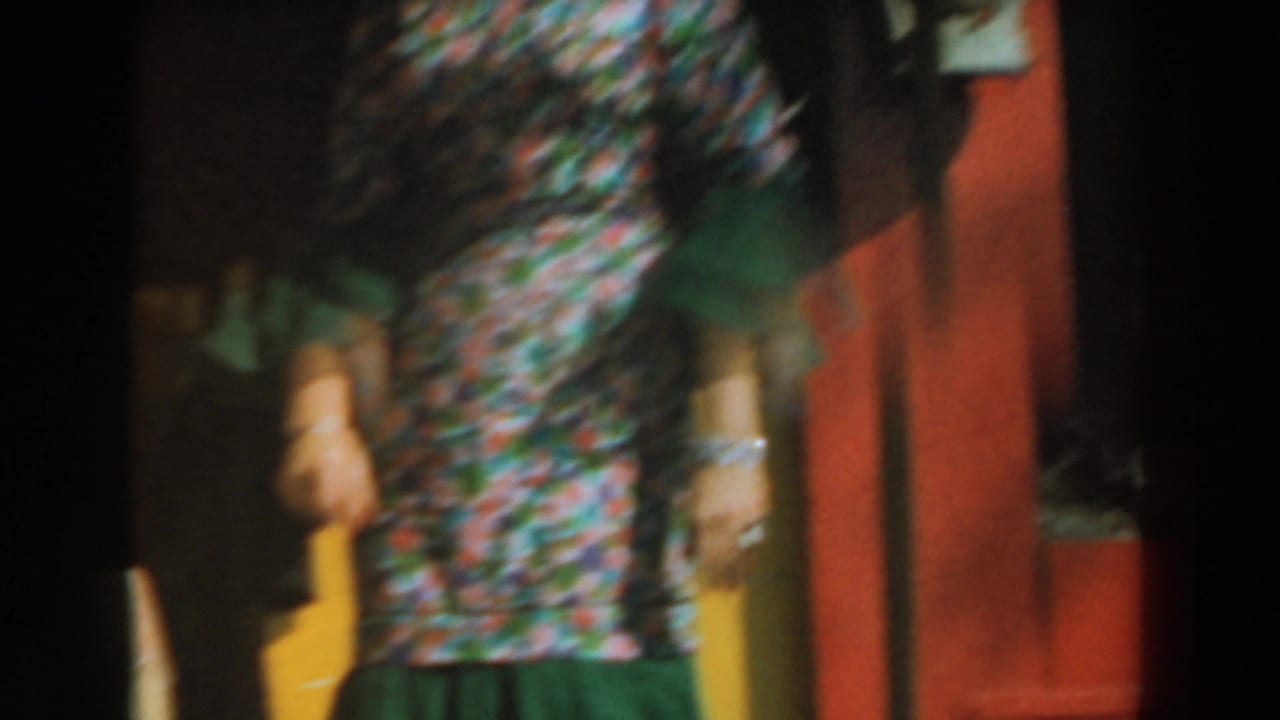 Blurred performer in floral clothing beside a red outdoor stage wall.