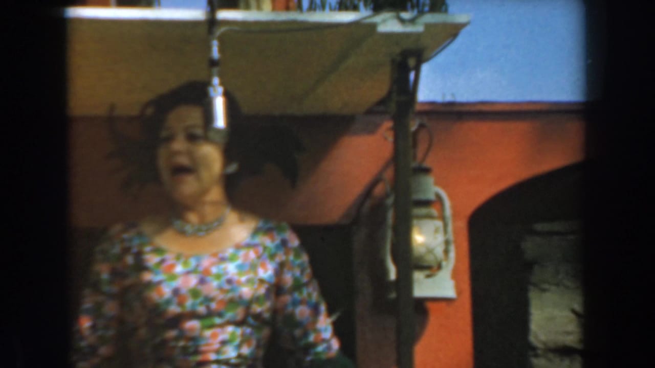 A woman in a colorful floral dress sings into a suspended microphone on an outdoor stage at Knott's Berry Farm in 1961.